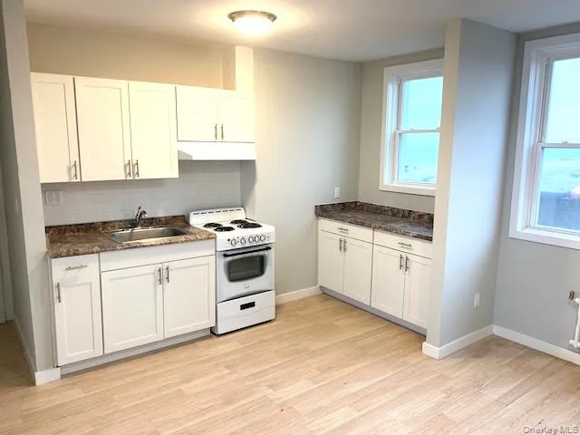 Kitchen featuring white range with electric cooktop, white cabinets, tasteful backsplash, and light wood-style floors Kitchen featuring white range with electric cooktop, white cabinets, tasteful backsplash, and light wood-style floors