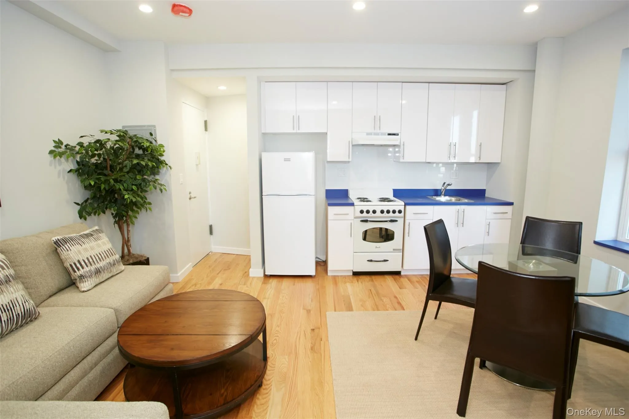 Kitchen featuring white cabinets, white appliances, light wood-type flooring, recessed lighting, and backsplash Kitchen featuring white cabinets, white appliances, light wood-type flooring, recessed lighting, and backsplash