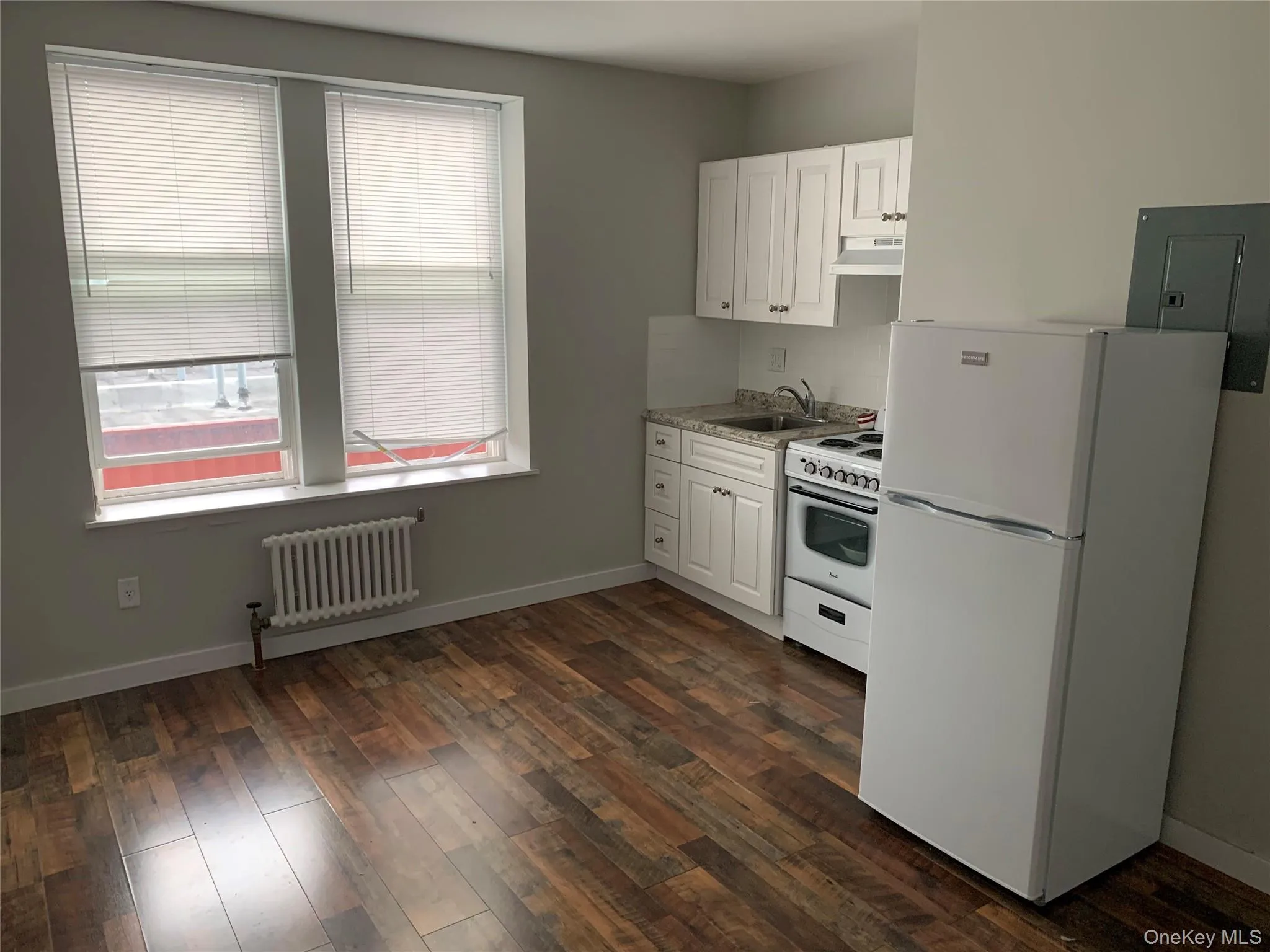 Kitchen with white appliances, white cabinets, radiator, and dark wood-style floors Kitchen with white appliances, white cabinets, radiator, and dark wood-style floors