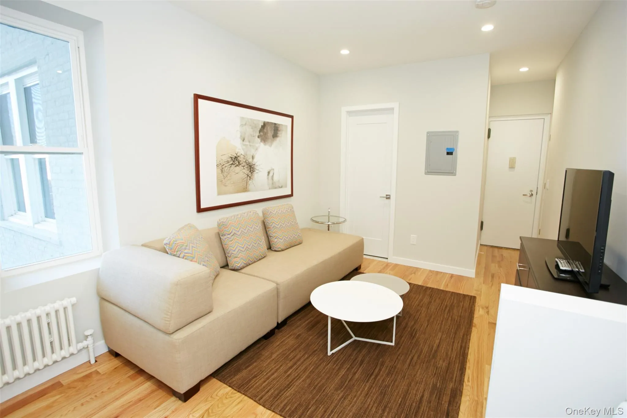 Living room with radiator, light wood finished floors, recessed lighting, and electric panel Living room with radiator, light wood finished floors, recessed lighting, and electric panel