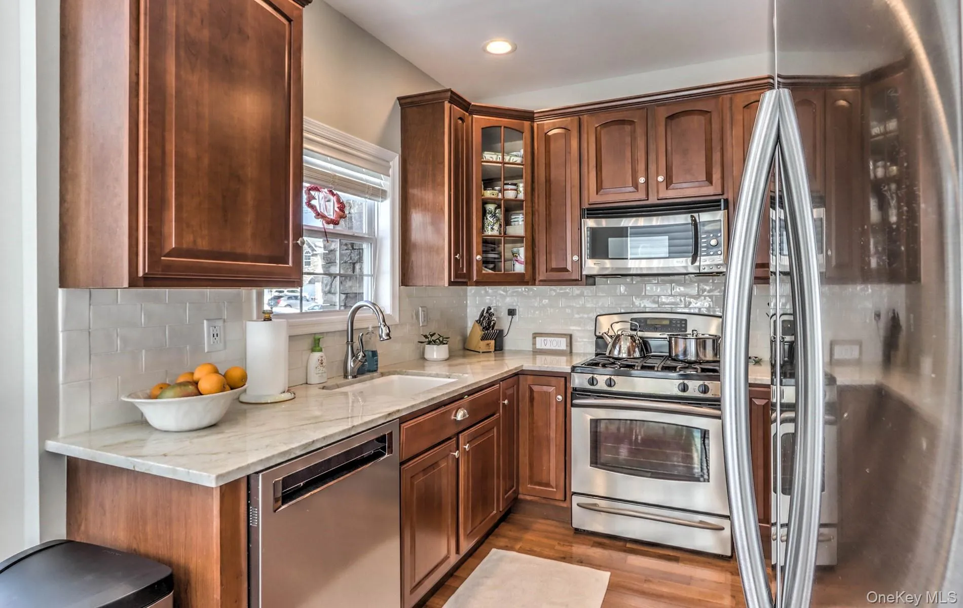 Kitchen featuring stainless steel appliances, light stone countertops, backsplash, light wood-style flooring, and glass insert cabinets Kitchen featuring stainless steel appliances, light stone countertops, backsplash, light wood-style flooring, and glass insert cabinets