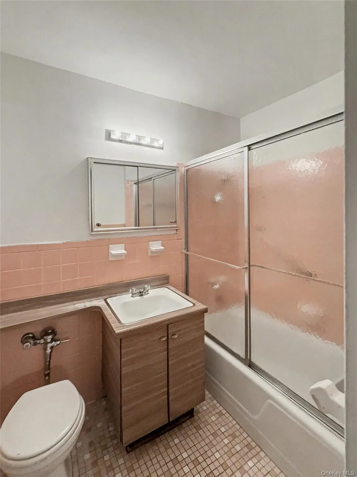 Bathroom with bath / shower combo with glass door, vanity, tile walls, and light tile patterned floors Bathroom with bath / shower combo with glass door, vanity, tile walls, and light tile patterned floors