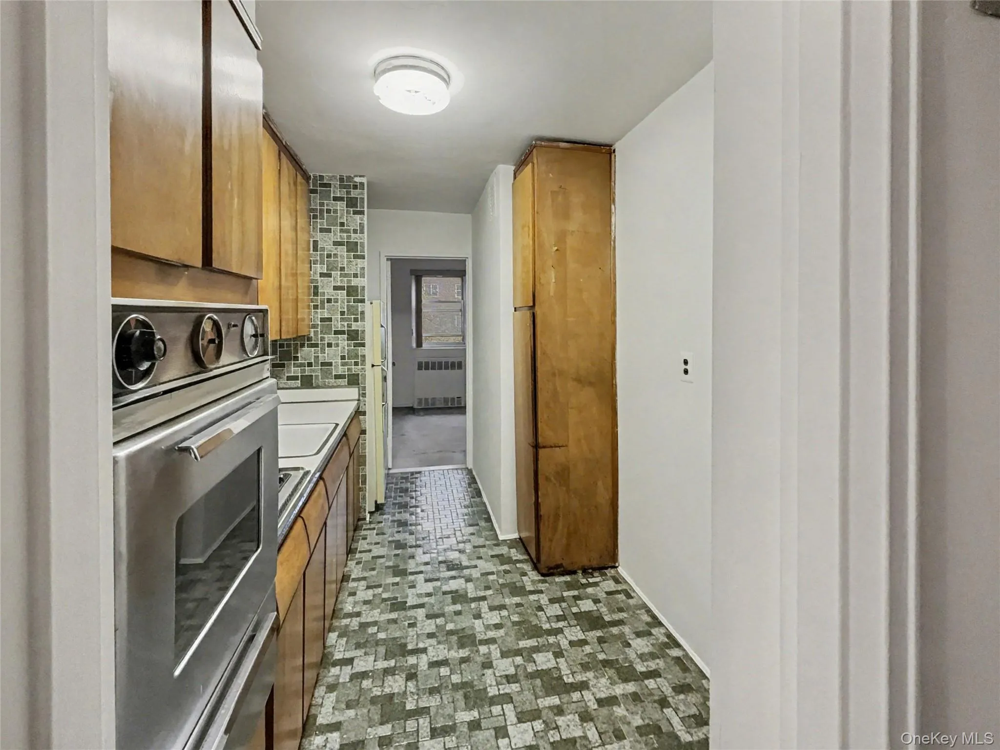 Kitchen featuring brown cabinetry, decorative backsplash, light countertops, and radiator Kitchen featuring brown cabinetry, decorative backsplash, light countertops, and radiator