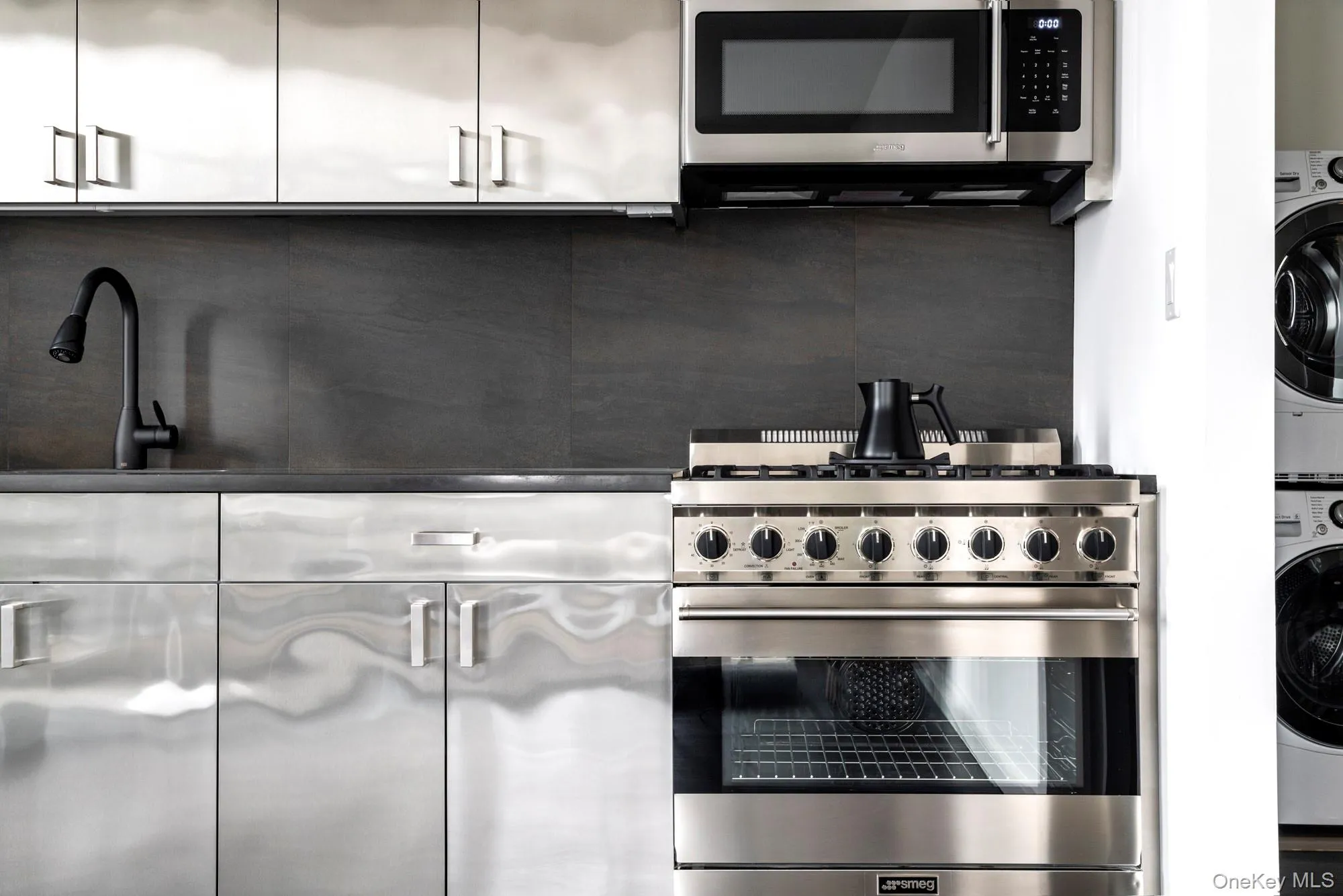 Kitchen featuring stainless steel appliances, white cabinets, and estacked washer and dryer Kitchen featuring stainless steel appliances, white cabinets, and estacked washer and dryer