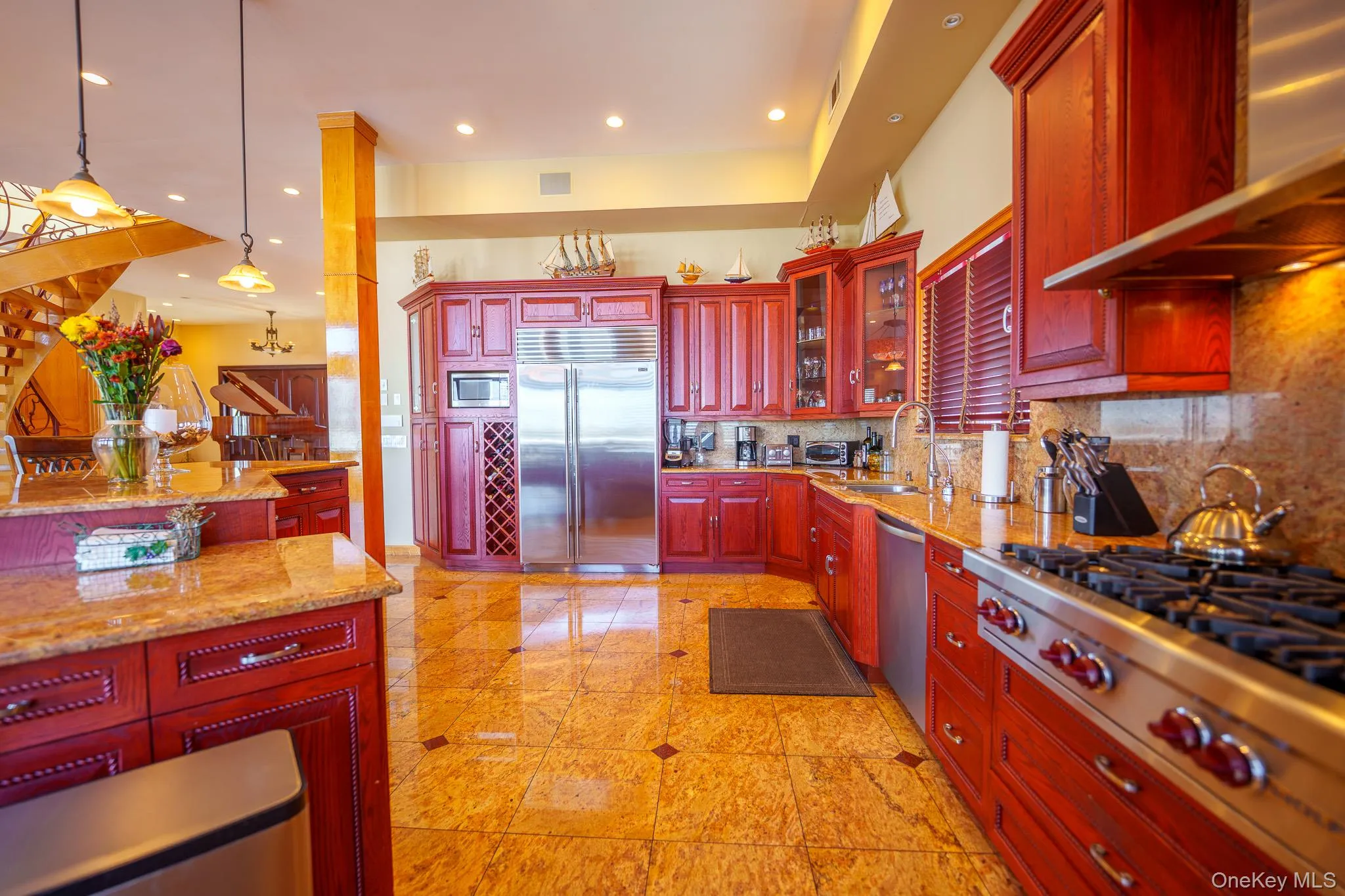 Kitchen featuring reddish brown cabinets, exhaust hood, light stone countertops, built in appliances, and recessed lighting Kitchen featuring reddish brown cabinets, exhaust hood, light stone countertops, built in appliances, and recessed lighting
