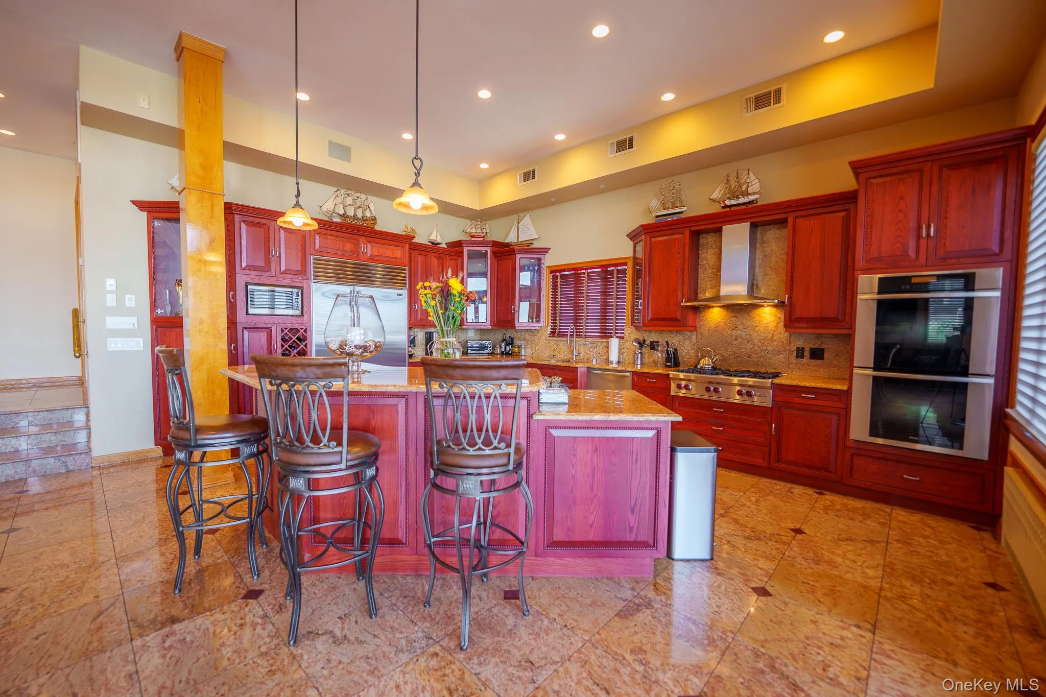Kitchen with appliances with stainless steel finishes, backsplash, light stone countertops, a center island, and decorative light fixtures Kitchen with appliances with stainless steel finishes, backsplash, light stone countertops, a center island, and decorative light fixtures