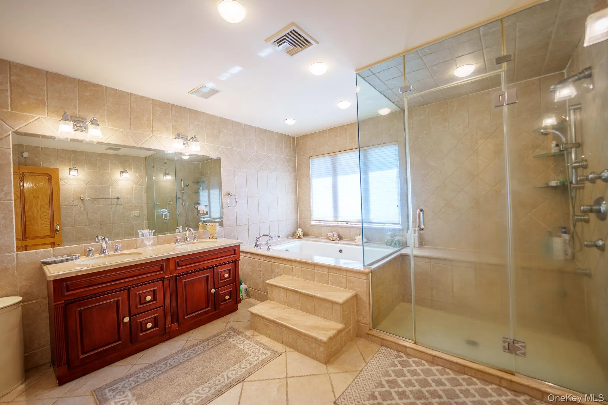 Bathroom featuring tile walls, a garden tub, double vanity, light tile patterned flooring, and a stall shower Bathroom featuring tile walls, a garden tub, double vanity, light tile patterned flooring, and a stall shower