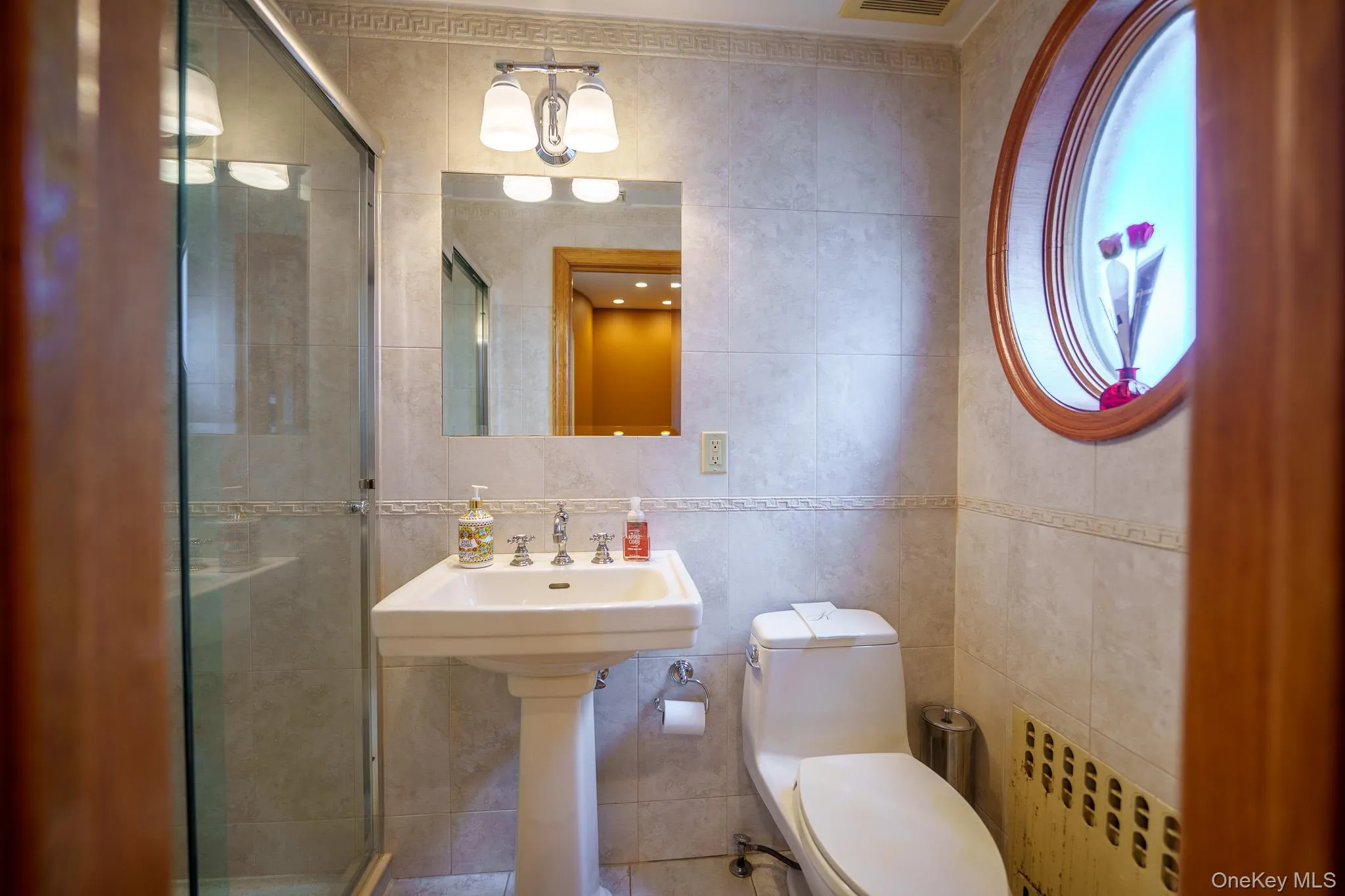 Bathroom featuring tile walls, radiator heating unit, a shower stall, tasteful backsplash, and a chandelier Bathroom featuring tile walls, radiator heating unit, a shower stall, tasteful backsplash, and a chandelier