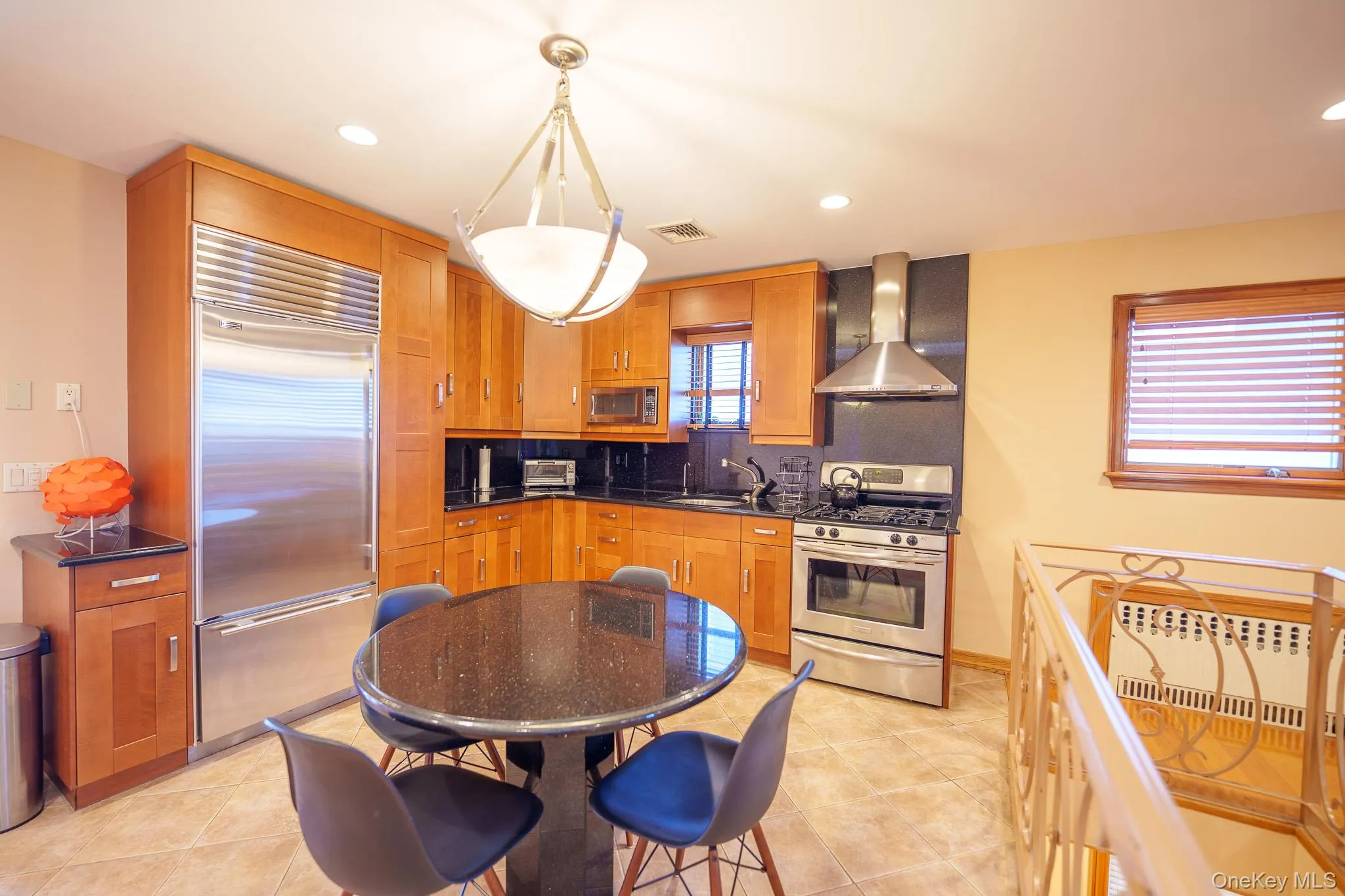 Kitchen with stainless steel appliances, decorative backsplash, radiator, wall chimney range hood, and brown cabinetry Kitchen with stainless steel appliances, decorative backsplash, radiator, wall chimney range hood, and brown cabinetry