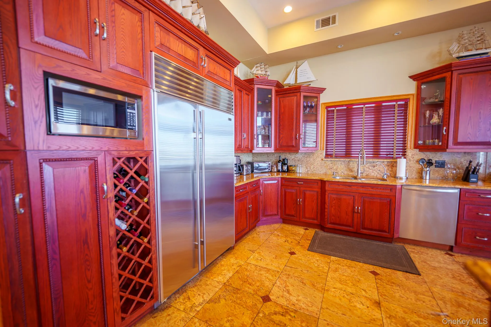 Kitchen featuring dark brown cabinets, stainless steel appliances, light stone countertops, tasteful backsplash, and glass insert cabinets Kitchen featuring dark brown cabinets, stainless steel appliances, light stone countertops, tasteful backsplash, and glass insert cabinets