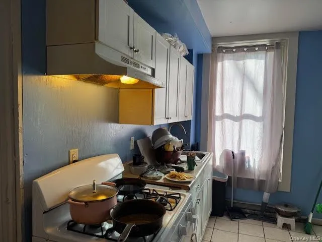 Kitchen with gas range oven, white cabinetry, light tile patterned floors, under cabinet range hood, and light countertops Kitchen with gas range oven, white cabinetry, light tile patterned floors, under cabinet range hood, and light countertops