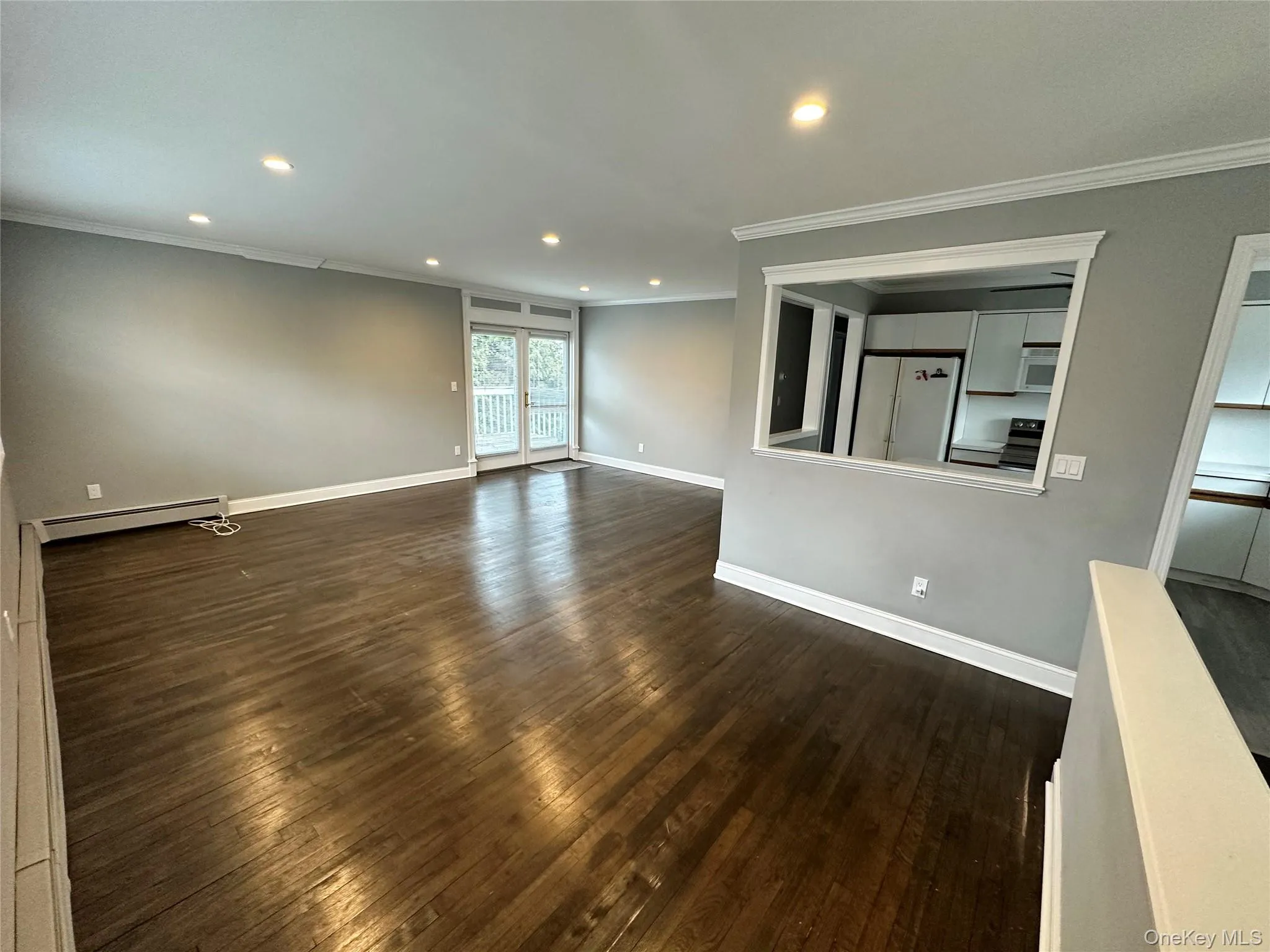 Unfurnished living room featuring ornamental molding, dark wood-style flooring, recessed lighting, and baseboard heating Unfurnished living room featuring ornamental molding, dark wood-style flooring, recessed lighting, and baseboard heating