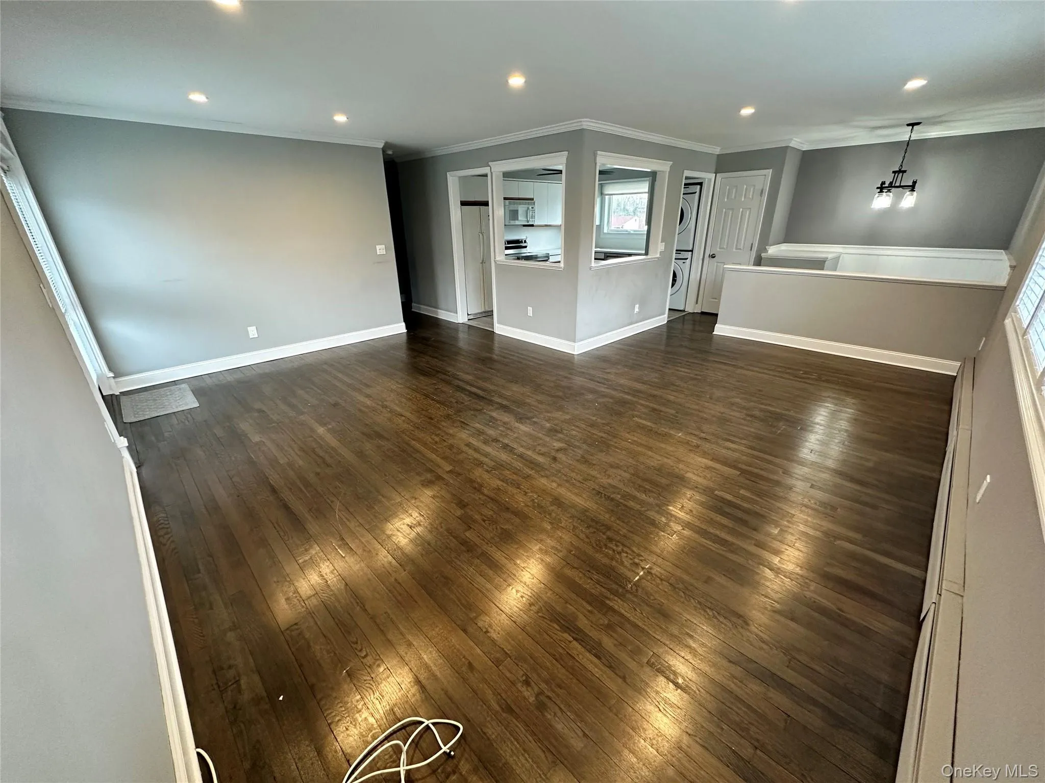 Unfurnished living room with dark wood-type flooring, recessed lighting, crown molding, a chandelier, and stacked washer and clothes dryer Unfurnished living room with dark wood-type flooring, recessed lighting, crown molding, a chandelier, and stacked washer and clothes dryer