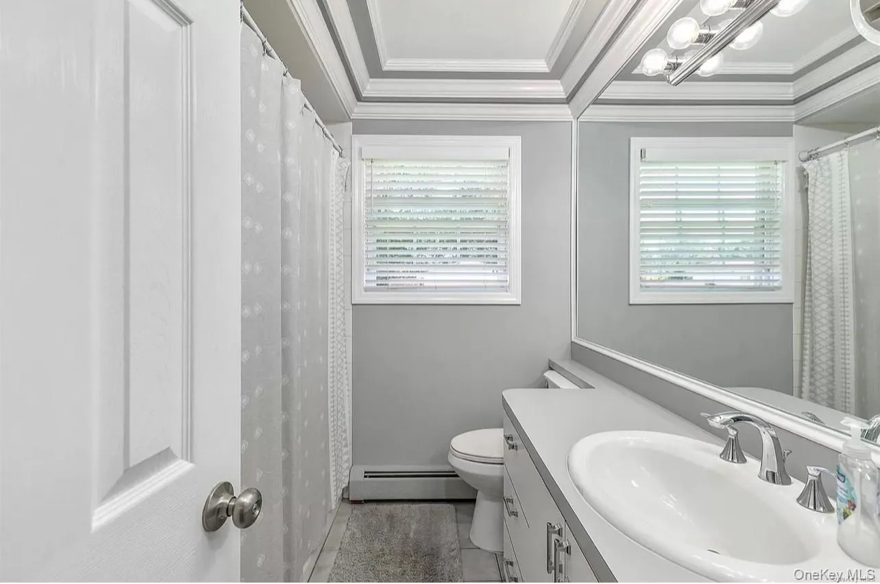Bathroom with a baseboard radiator, vanity, light tile patterned flooring, crown molding, and plenty of natural light Bathroom with a baseboard radiator, vanity, light tile patterned flooring, crown molding, and plenty of natural light