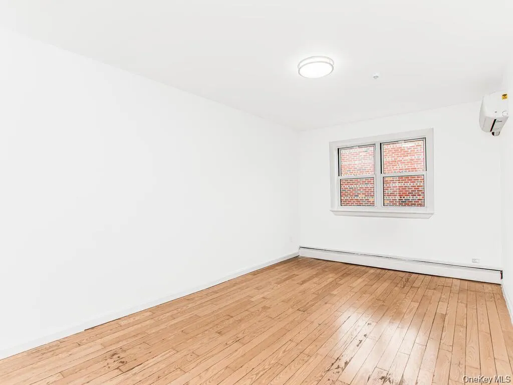 Unfurnished room featuring light wood-style floors, baseboard heating, and a wall unit AC Unfurnished room featuring light wood-style floors, baseboard heating, and a wall unit AC