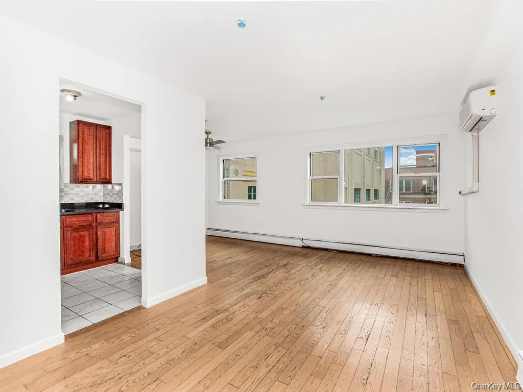 Unfurnished room with light wood-style floors, baseboard heating, ceiling fan, and a wall mounted air conditioner Unfurnished room with light wood-style floors, baseboard heating, ceiling fan, and a wall mounted air conditioner