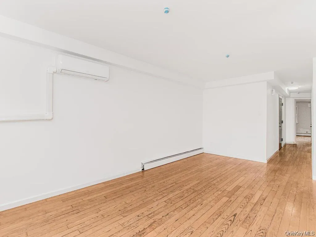 Empty room with light wood-type flooring, a baseboard heating unit, and an AC wall unit Empty room with light wood-type flooring, a baseboard heating unit, and an AC wall unit