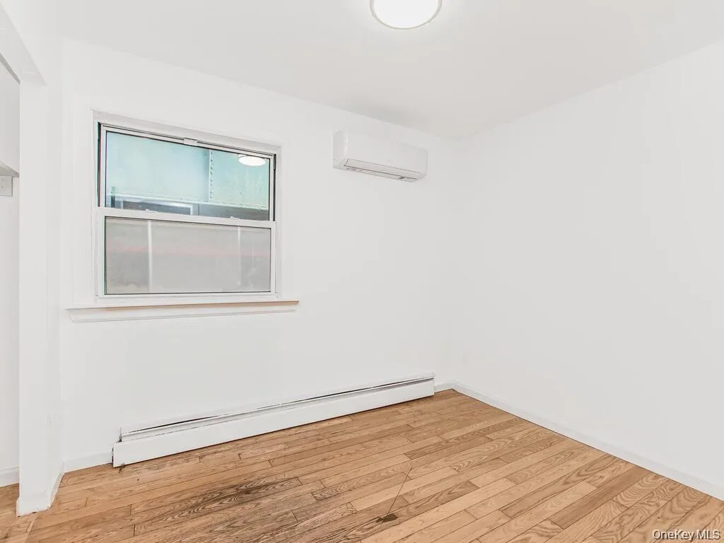 Unfurnished room with a baseboard radiator, light wood-style flooring, and a wall mounted AC Unfurnished room with a baseboard radiator, light wood-style flooring, and a wall mounted AC