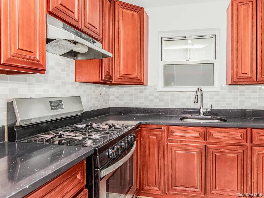 Kitchen featuring stainless steel gas range oven, under cabinet range hood, tasteful backsplash, and dark stone counters Kitchen featuring stainless steel gas range oven, under cabinet range hood, tasteful backsplash, and dark stone counters