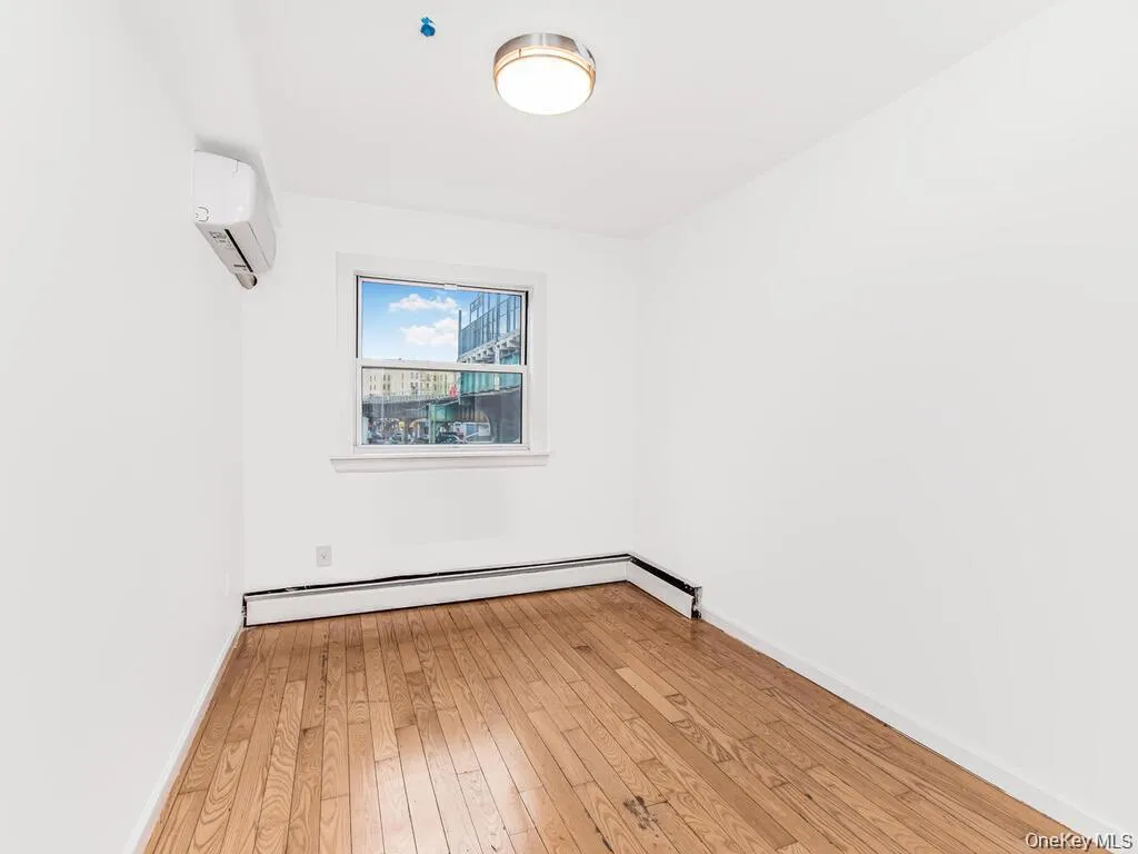 Empty room with light wood-style flooring, a wall mounted air conditioner, and a baseboard radiator Empty room with light wood-style flooring, a wall mounted air conditioner, and a baseboard radiator