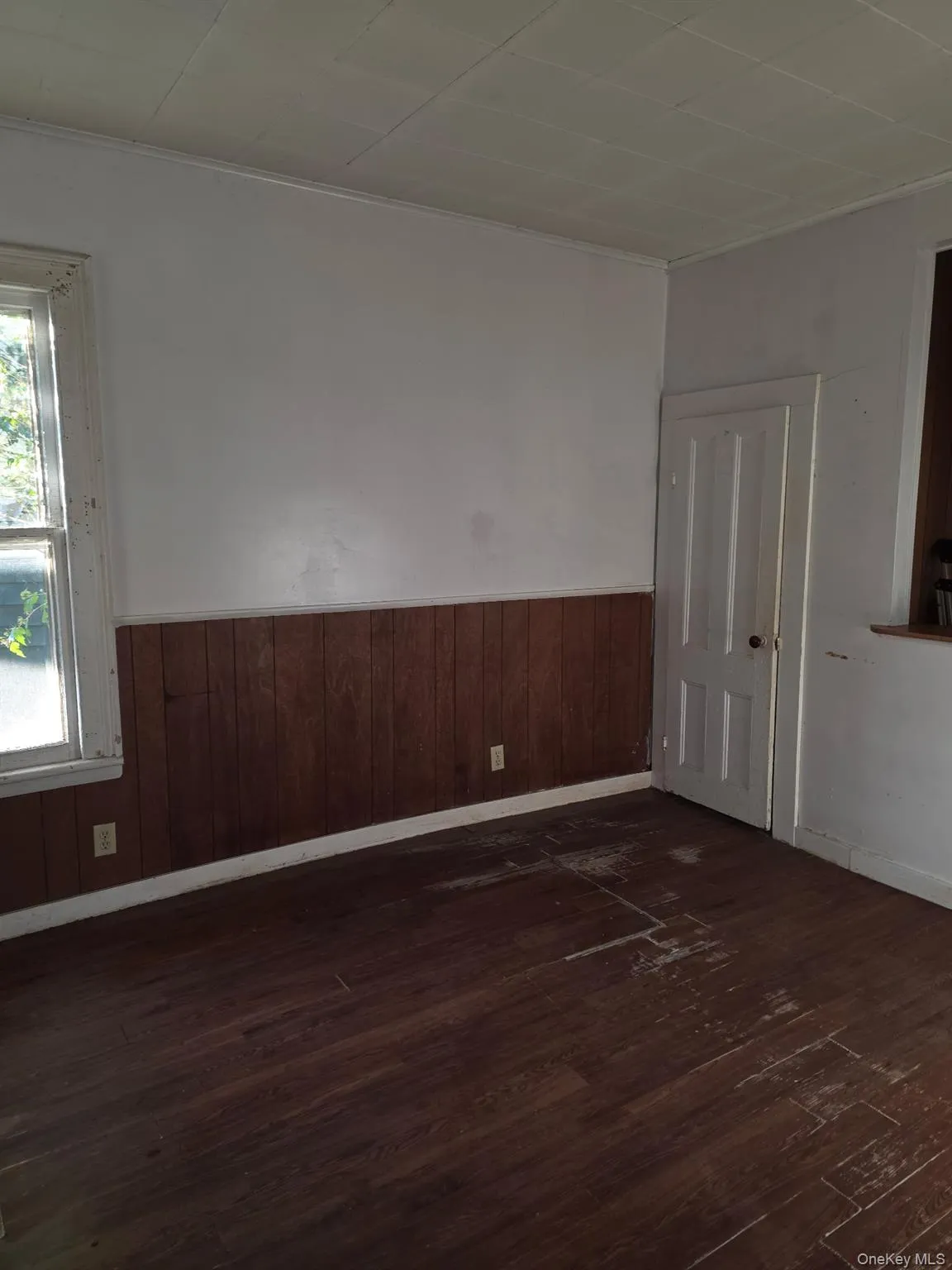 Unfurnished room featuring dark wood-type flooring, ornamental molding, and a wainscoted wall Unfurnished room featuring dark wood-type flooring, ornamental molding, and a wainscoted wall