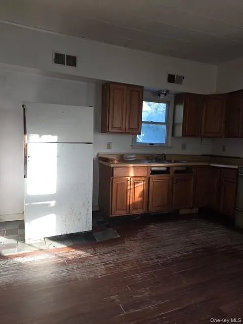 Kitchen featuring freestanding refrigerator, brown cabinetry, light countertops, and dark wood-style flooring Kitchen featuring freestanding refrigerator, brown cabinetry, light countertops, and dark wood-style flooring