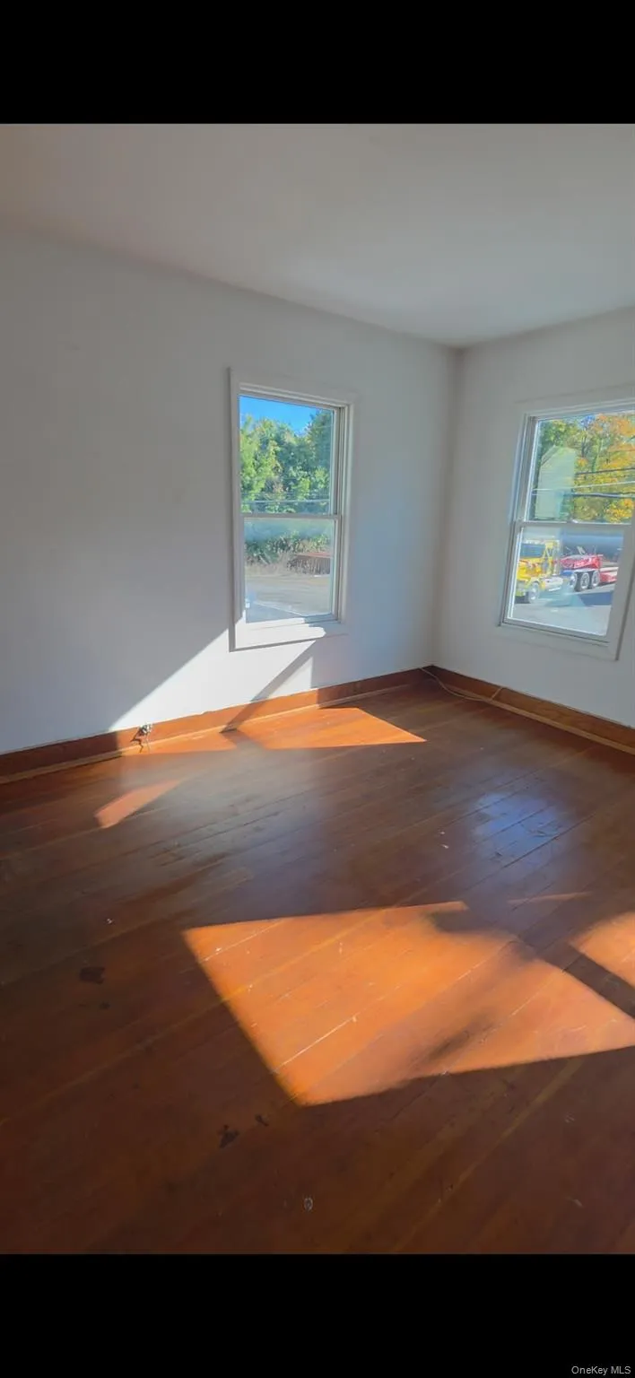 Spare room with dark wood-style flooring and healthy amount of natural light Spare room with dark wood-style flooring and healthy amount of natural light