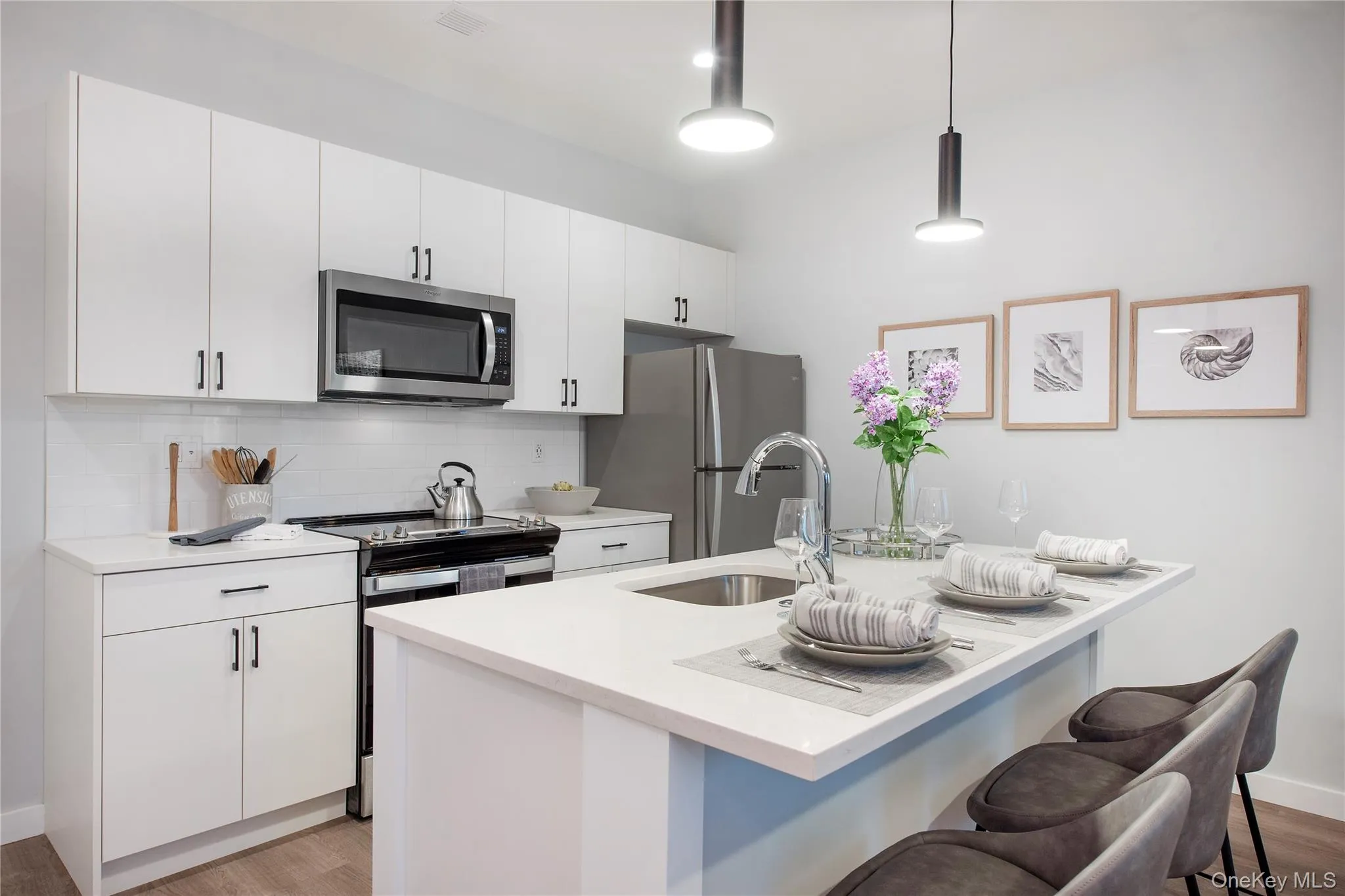 Kitchen with appliances with stainless steel finishes, light wood-style floors, a breakfast bar, decorative backsplash, and white cabinets Kitchen with appliances with stainless steel finishes, light wood-style floors, a breakfast bar, decorative backsplash, and white cabinets