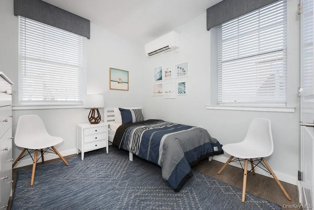 Bedroom with a wall mounted AC, multiple windows, and dark wood-type flooring Bedroom with a wall mounted AC, multiple windows, and dark wood-type flooring