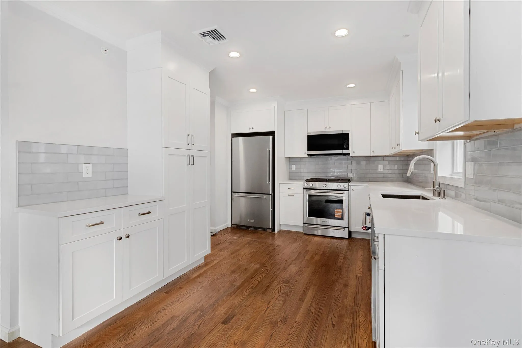 Kitchen with appliances with stainless steel finishes, white cabinets, light stone countertops, backsplash, and recessed lighting Kitchen with appliances with stainless steel finishes, white cabinets, light stone countertops, backsplash, and recessed lighting