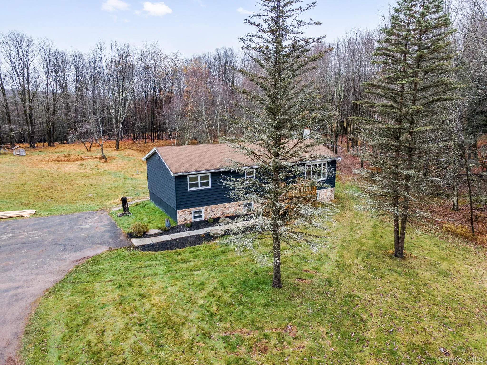 Ranch-style home featuring stone siding, a front lawn, and a view of trees Ranch-style home featuring stone siding, a front lawn, and a view of trees