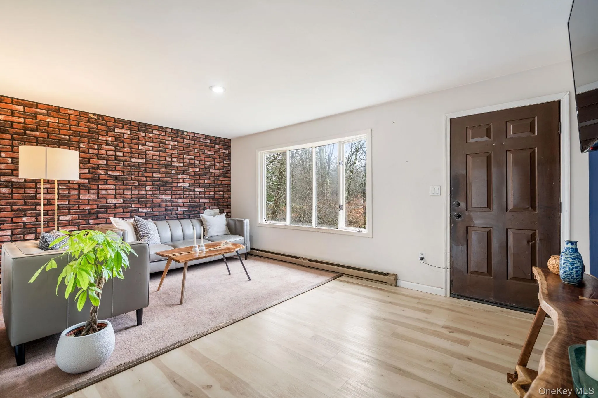 Living room featuring brick wall, a baseboard radiator, an accent wall, and wood finished floors Living room featuring brick wall, a baseboard radiator, an accent wall, and wood finished floors