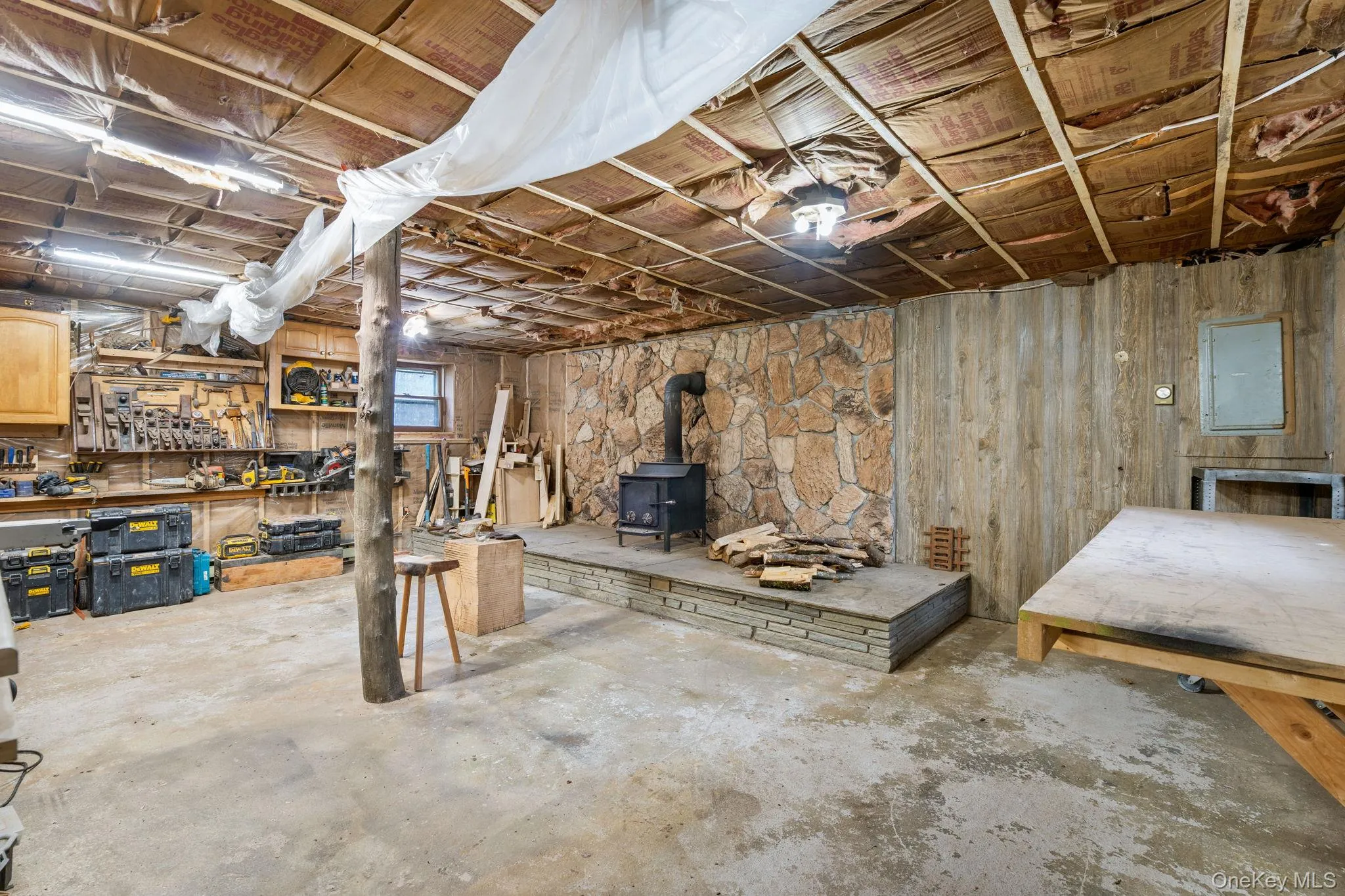 Below grade area featuring a wood stove, a workshop area, and wooden walls Below grade area featuring a wood stove, a workshop area, and wooden walls