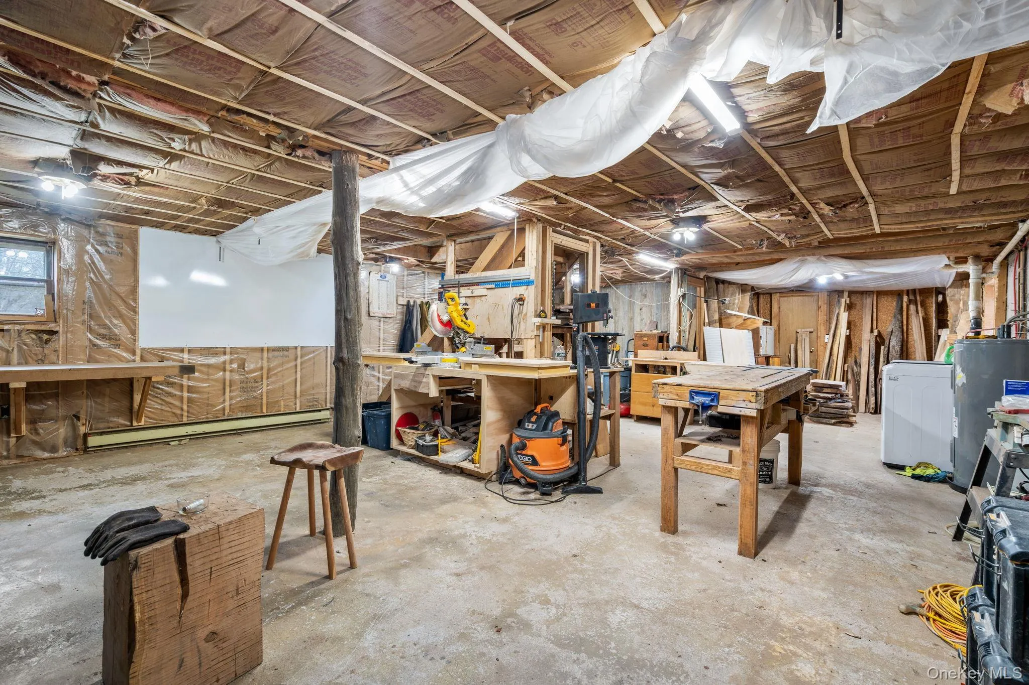 Unfinished below grade area featuring a workshop area, water heater, a baseboard radiator, and washer / dryer Unfinished below grade area featuring a workshop area, water heater, a baseboard radiator, and washer / dryer