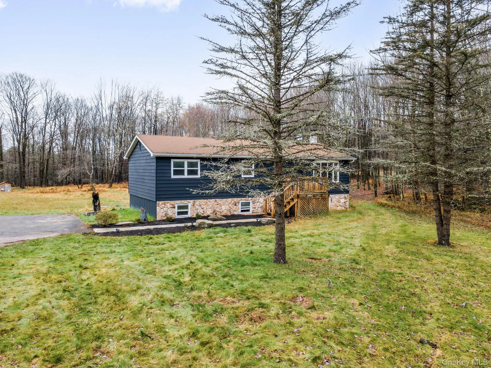 View of front of home featuring a front yard, a wooden deck, stone siding, and stairs View of front of home featuring a front yard, a wooden deck, stone siding, and stairs