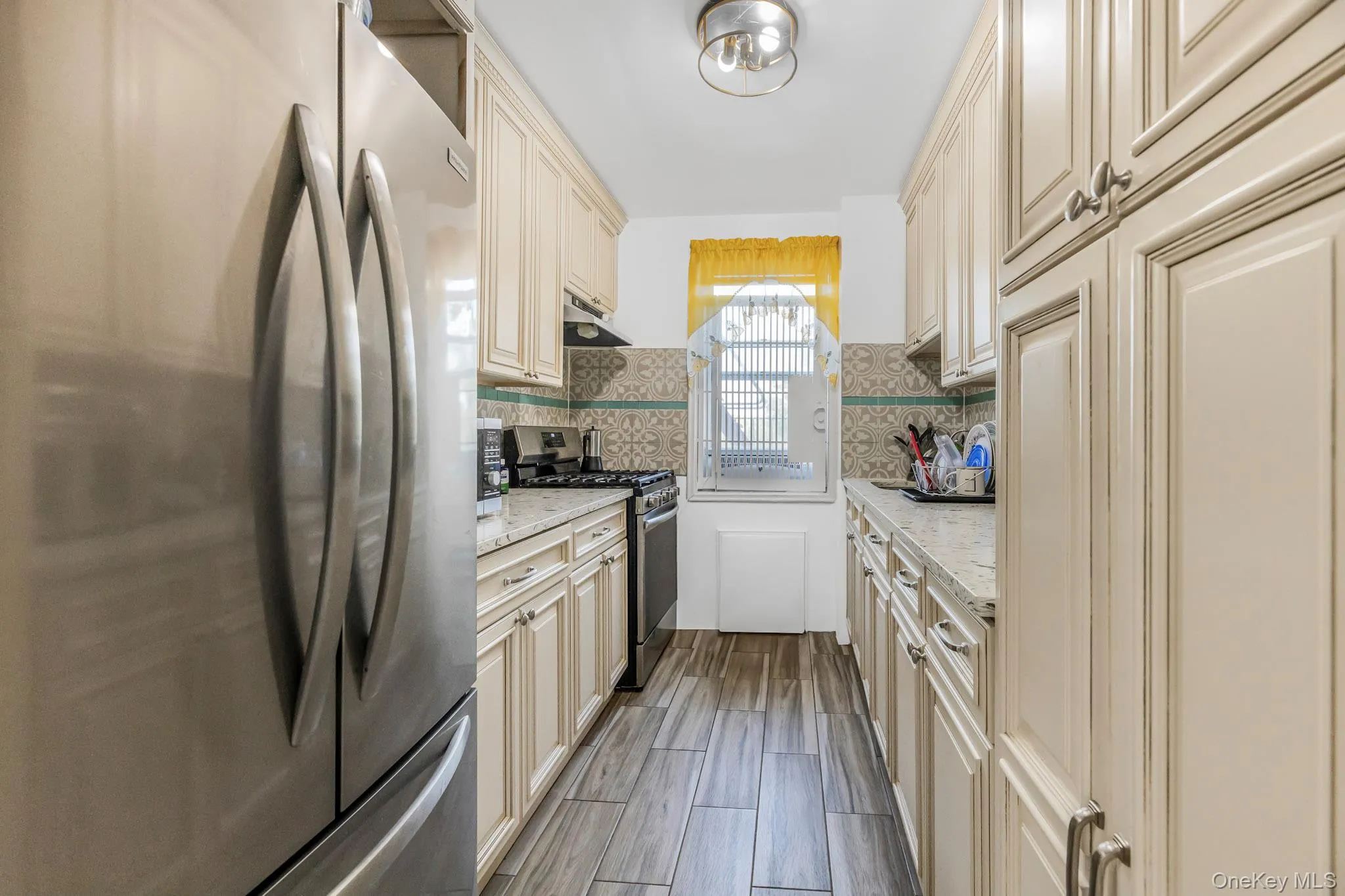Kitchen with cream cabinetry, stainless steel appliances, light stone counters, decorative backsplash, and wood finish floors Kitchen with cream cabinetry, stainless steel appliances, light stone counters, decorative backsplash, and wood finish floors