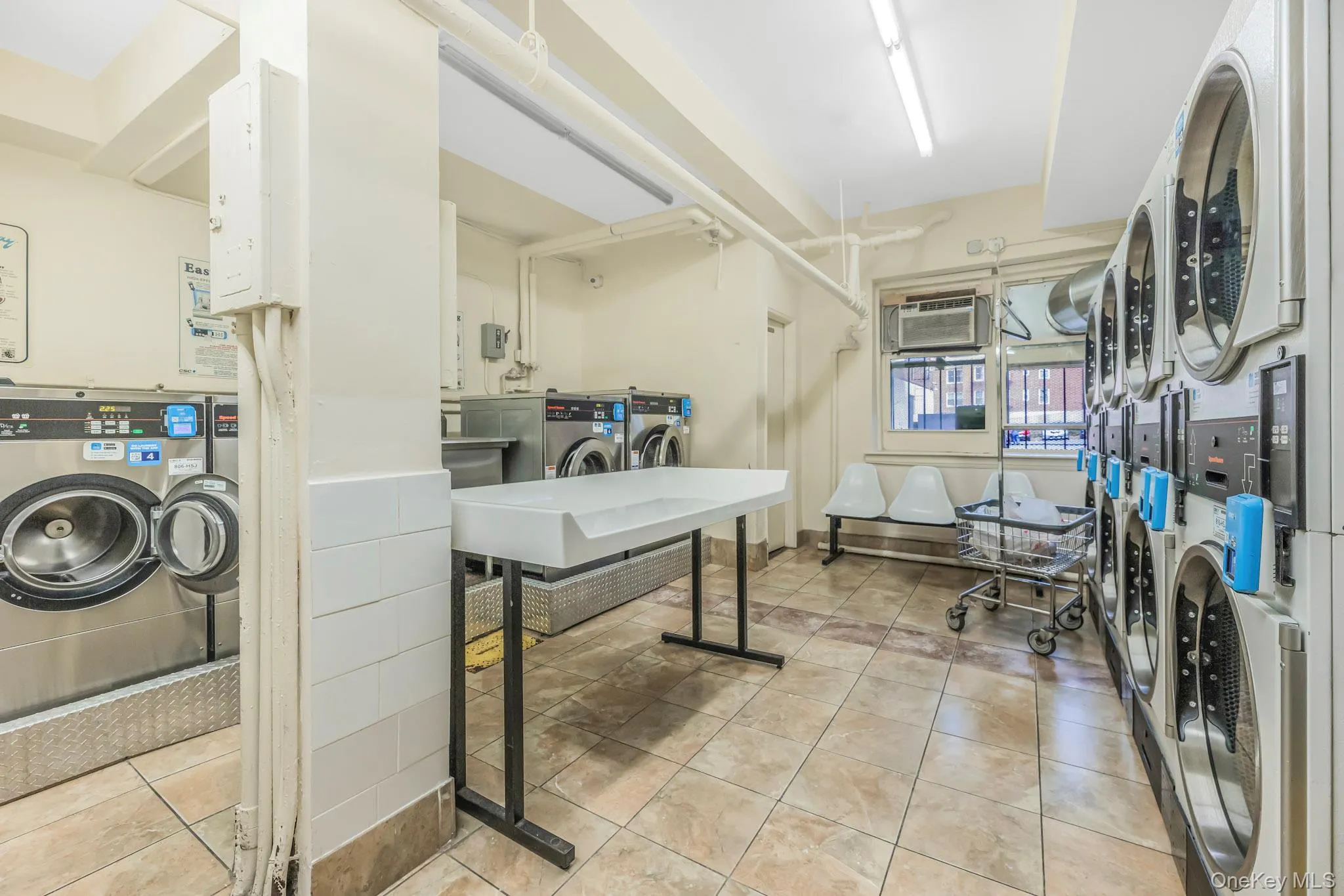 Communal laundry room with separate washer and dryer, water heater, estacked washer and dryer, and a wall unit AC Communal laundry room with separate washer and dryer, water heater, estacked washer and dryer, and a wall unit AC
