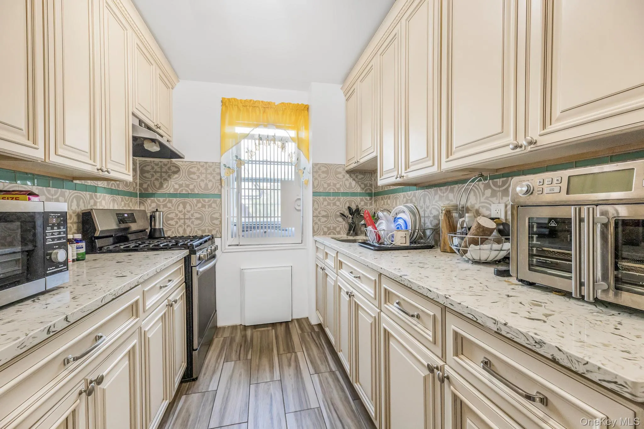 Kitchen with cream cabinets, stainless steel appliances, light stone countertops, under cabinet range hood, and wood tiled floors Kitchen with cream cabinets, stainless steel appliances, light stone countertops, under cabinet range hood, and wood tiled floors