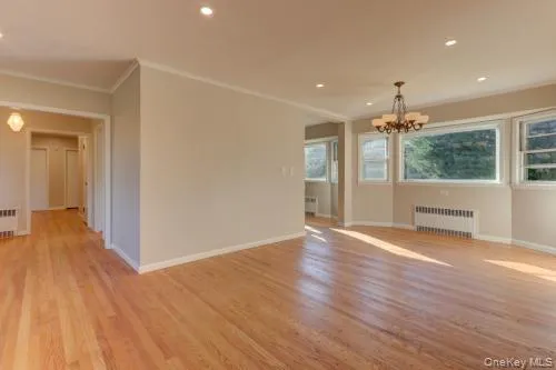 Empty room with recessed lighting, light wood-style flooring, radiator heating unit, and a chandelier Empty room with recessed lighting, light wood-style flooring, radiator heating unit, and a chandelier