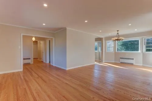 Unfurnished room featuring light wood finished floors, recessed lighting, radiator, a chandelier, and crown molding Unfurnished room featuring light wood finished floors, recessed lighting, radiator, a chandelier, and crown molding