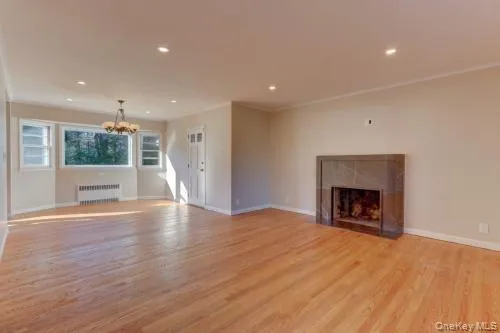 Unfurnished living room featuring light wood-style floors, a fireplace, recessed lighting, crown molding, and radiator heating unit Unfurnished living room featuring light wood-style floors, a fireplace, recessed lighting, crown molding, and radiator heating unit