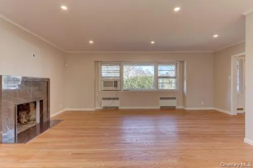 Unfurnished living room with ornamental molding, light wood-style flooring, a fireplace, recessed lighting, and radiator Unfurnished living room with ornamental molding, light wood-style flooring, a fireplace, recessed lighting, and radiator