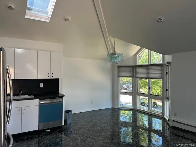Kitchen featuring white cabinets, dark countertops, stainless steel appliances, a skylight, and pendant lighting Kitchen featuring white cabinets, dark countertops, stainless steel appliances, a skylight, and pendant lighting