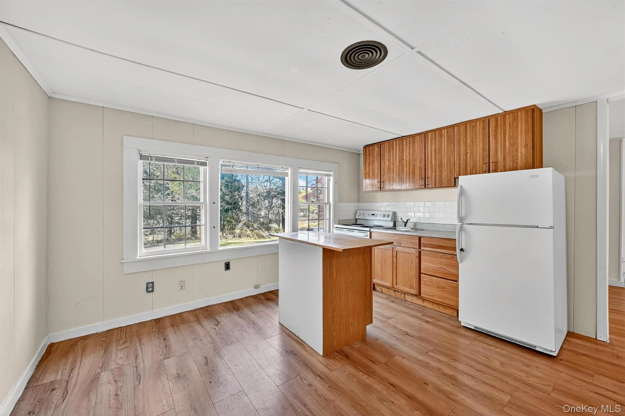 Kitchen with white appliances, light wood finished floors, tasteful backsplash, a kitchen island, and brown cabinets Kitchen with white appliances, light wood finished floors, tasteful backsplash, a kitchen island, and brown cabinets