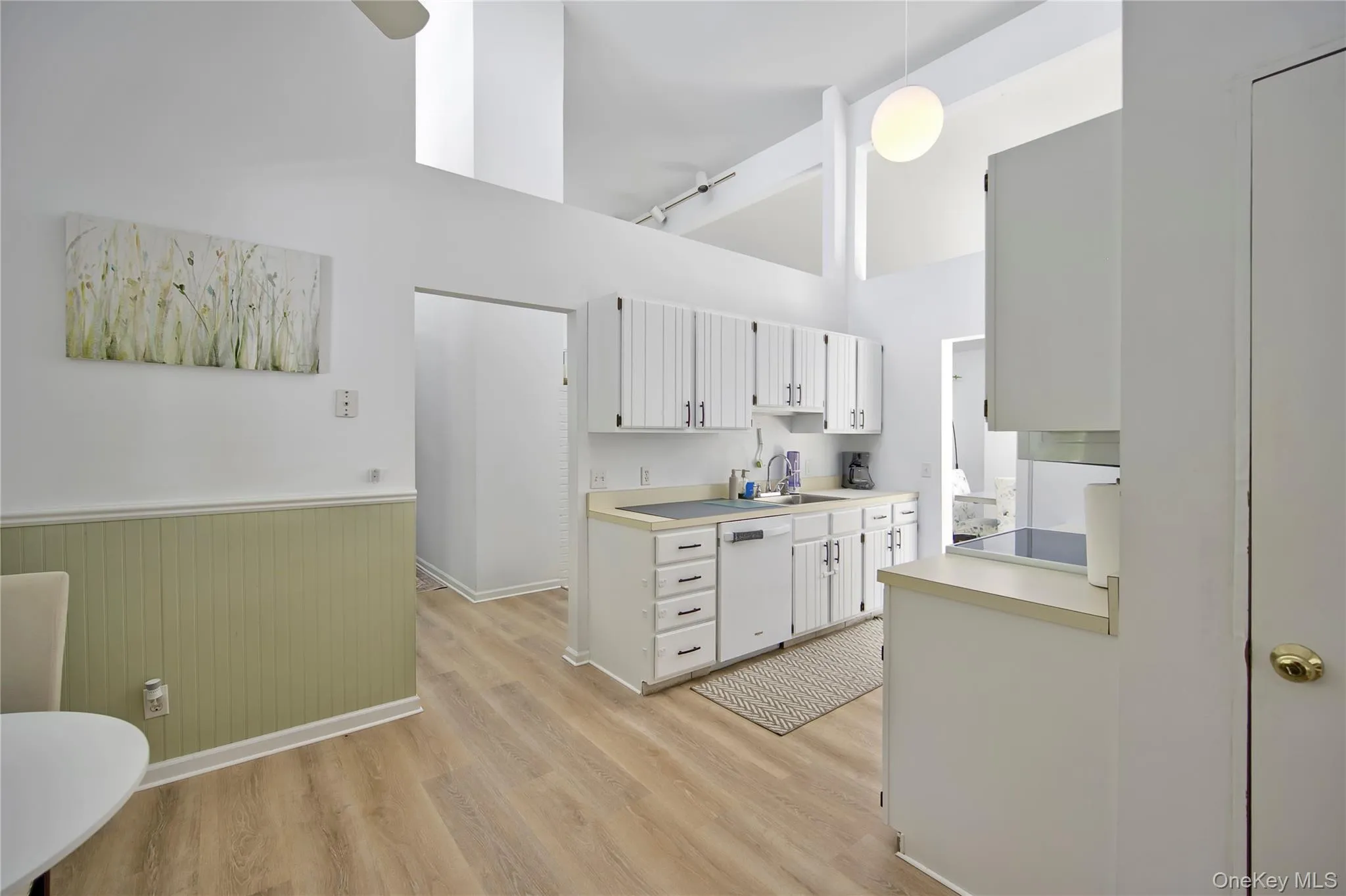 Kitchen with light countertops, wainscoting, a high ceiling, light wood-style floors, and dishwasher Kitchen with light countertops, wainscoting, a high ceiling, light wood-style floors, and dishwasher