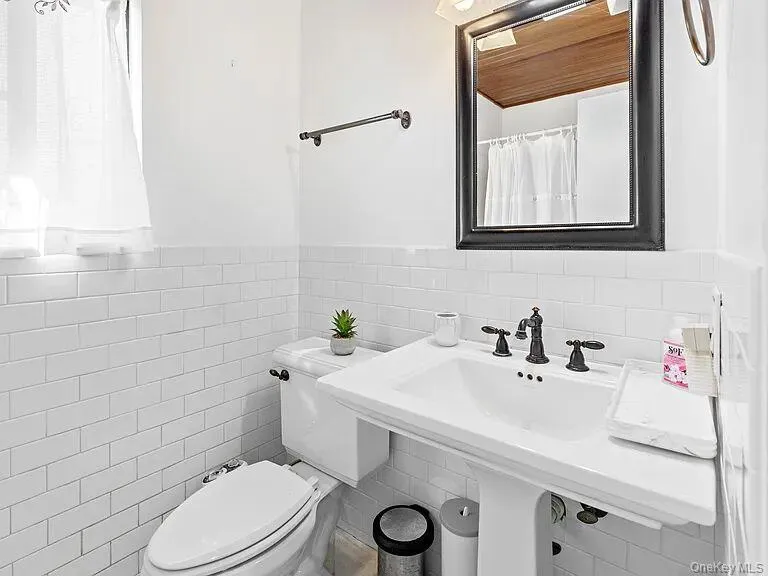 Full bathroom with tile walls, wainscoting, and curtained shower Full bathroom with tile walls, wainscoting, and curtained shower