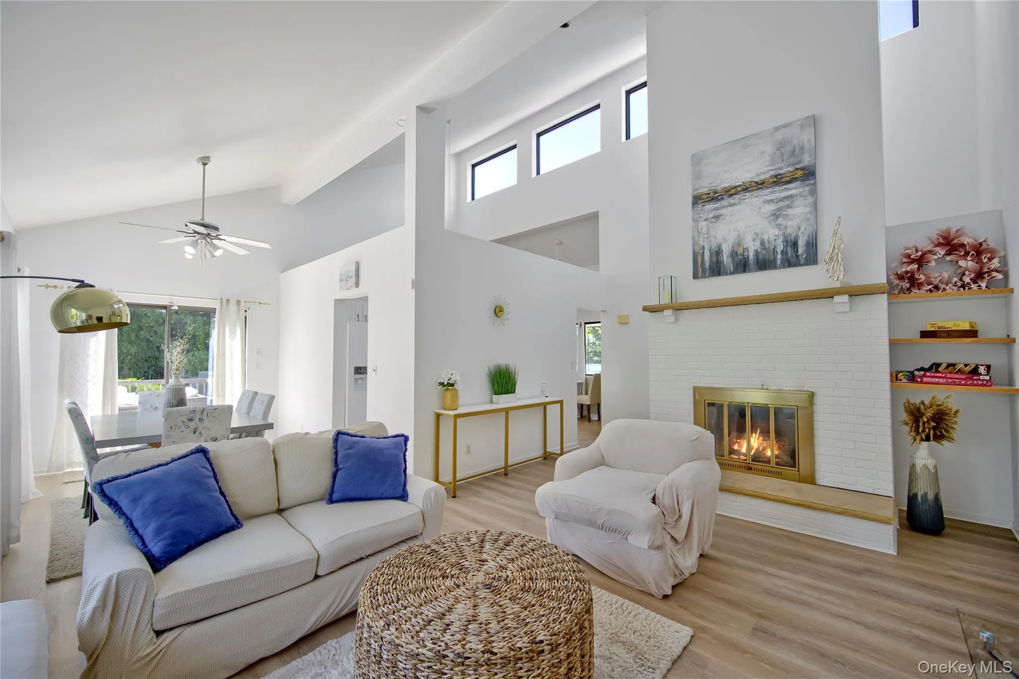 Living area featuring plenty of natural light, high vaulted ceiling, wood finished floors, a fireplace, and ceiling fan Living area featuring plenty of natural light, high vaulted ceiling, wood finished floors, a fireplace, and ceiling fan