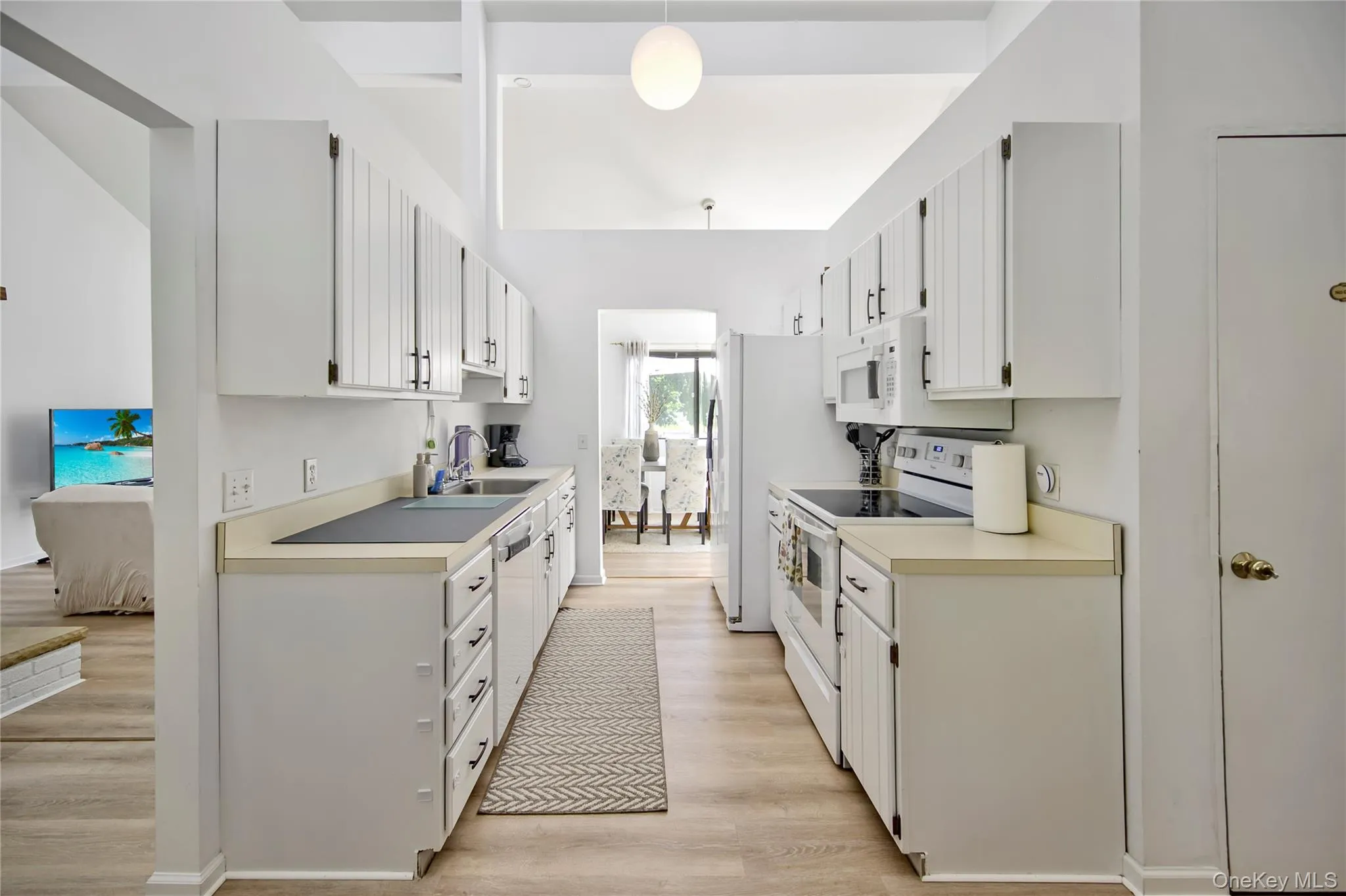 Kitchen featuring white appliances, light wood-style flooring, light countertops, white cabinetry, and decorative light fixtures Kitchen featuring white appliances, light wood-style flooring, light countertops, white cabinetry, and decorative light fixtures