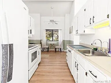 Kitchen with light wood finished floors, white cabinetry, white appliances, light countertops, and ceiling fan Kitchen with light wood finished floors, white cabinetry, white appliances, light countertops, and ceiling fan