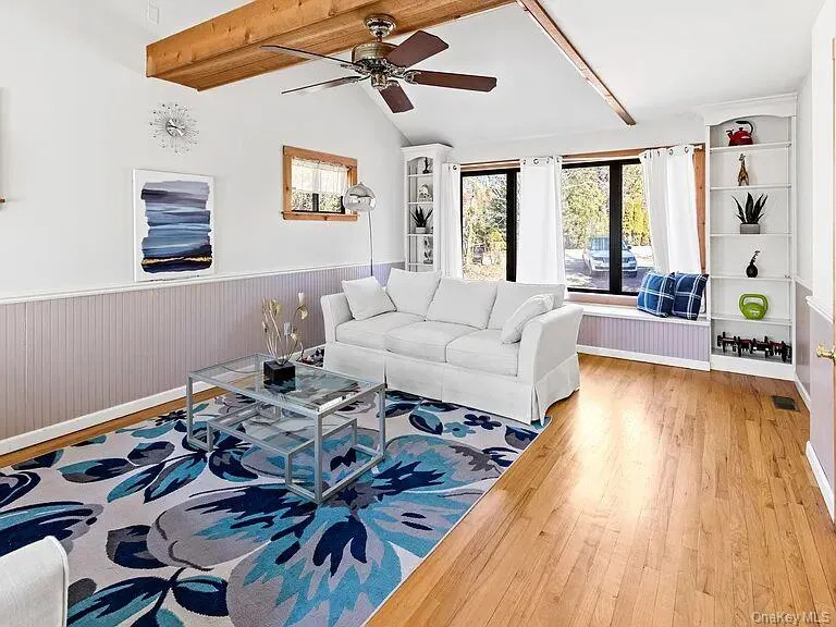 Living area with wood finished floors, a ceiling fan, built in features, and a wainscoted wall Living area with wood finished floors, a ceiling fan, built in features, and a wainscoted wall